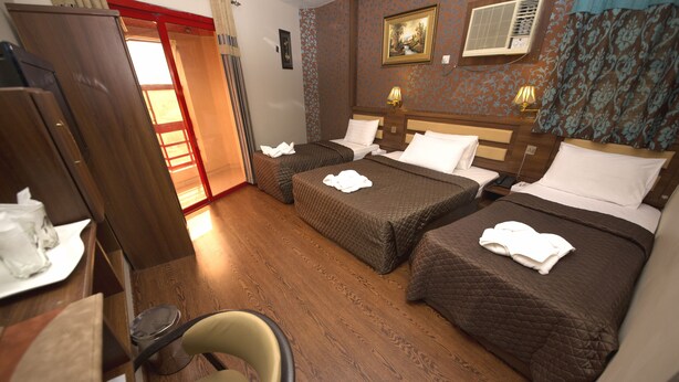 A hotel room with two beds, a wooden floor, a chair, a desk with a lamp, and a painting on the wall. - Downtown Hotel (Dubai)