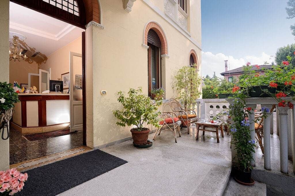 L’entrée d’un hôtel, avec un comptoir d’accueil, des plantes en pot et des sièges à l’extérieur.