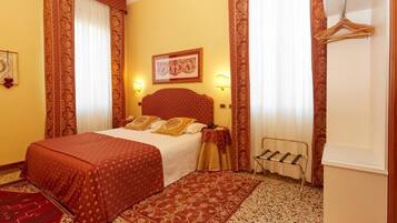 Camera d'albergo con un letto grande, due lampade a parete, un appendiabiti e un piccolo tavolo con una sedia.