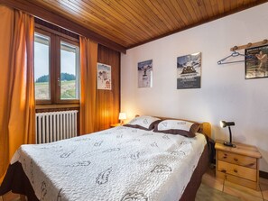 Relax in this serene bedroom with a plush bed, adorned with a leaf-patterned quilt, and enjoy the natural light pouring in through the large window.