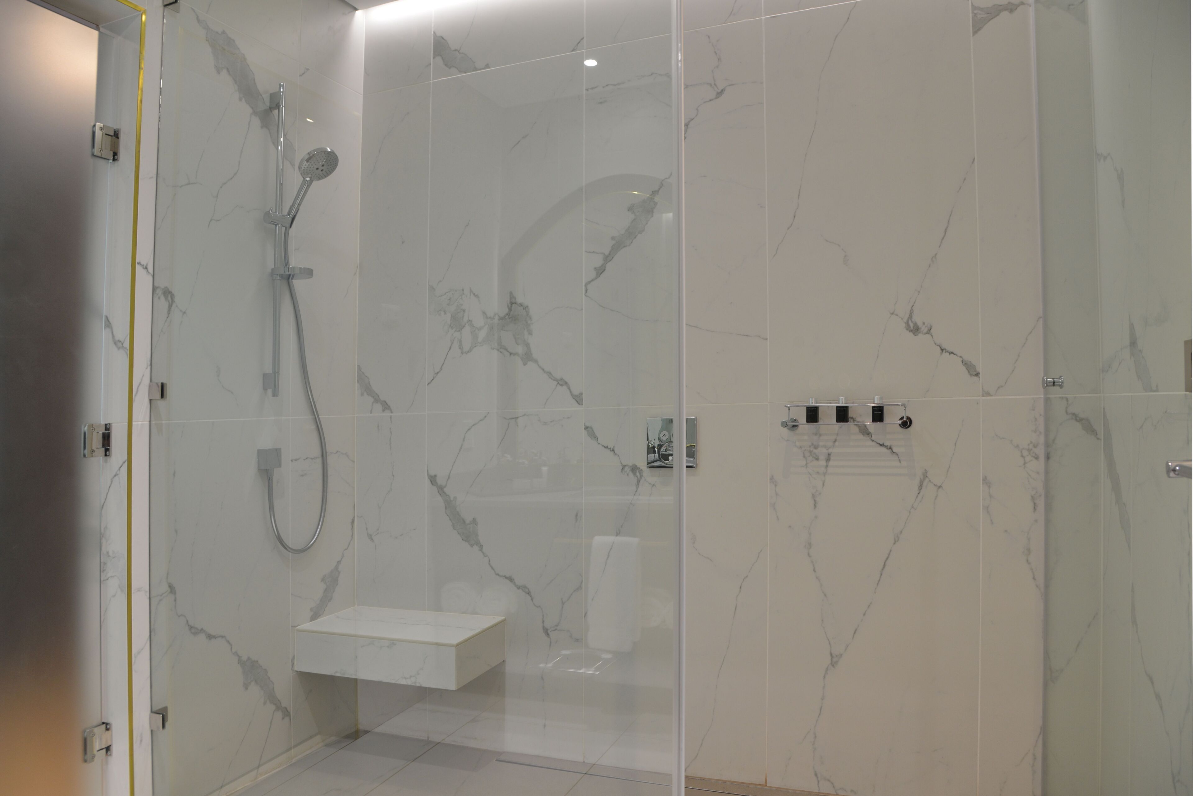 A modern bathroom with a glass-enclosed shower, marble walls, and a built-in sink.