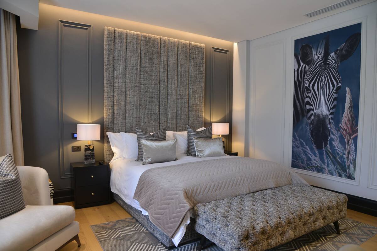 A modern hotel room with a large bed, a nightstand with a lamp, a sofa, and a zebra painting on the wall.