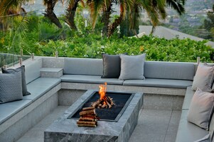 Un área de estar moderna al aire libre con una chimenea integrada y vistas a vegetación exuberante.