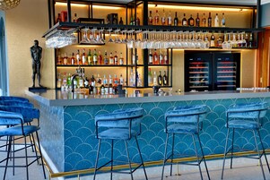 Zona de bar con pared de azulejos azules, múltiples estantes llenos de botellas de licor y taburetes.