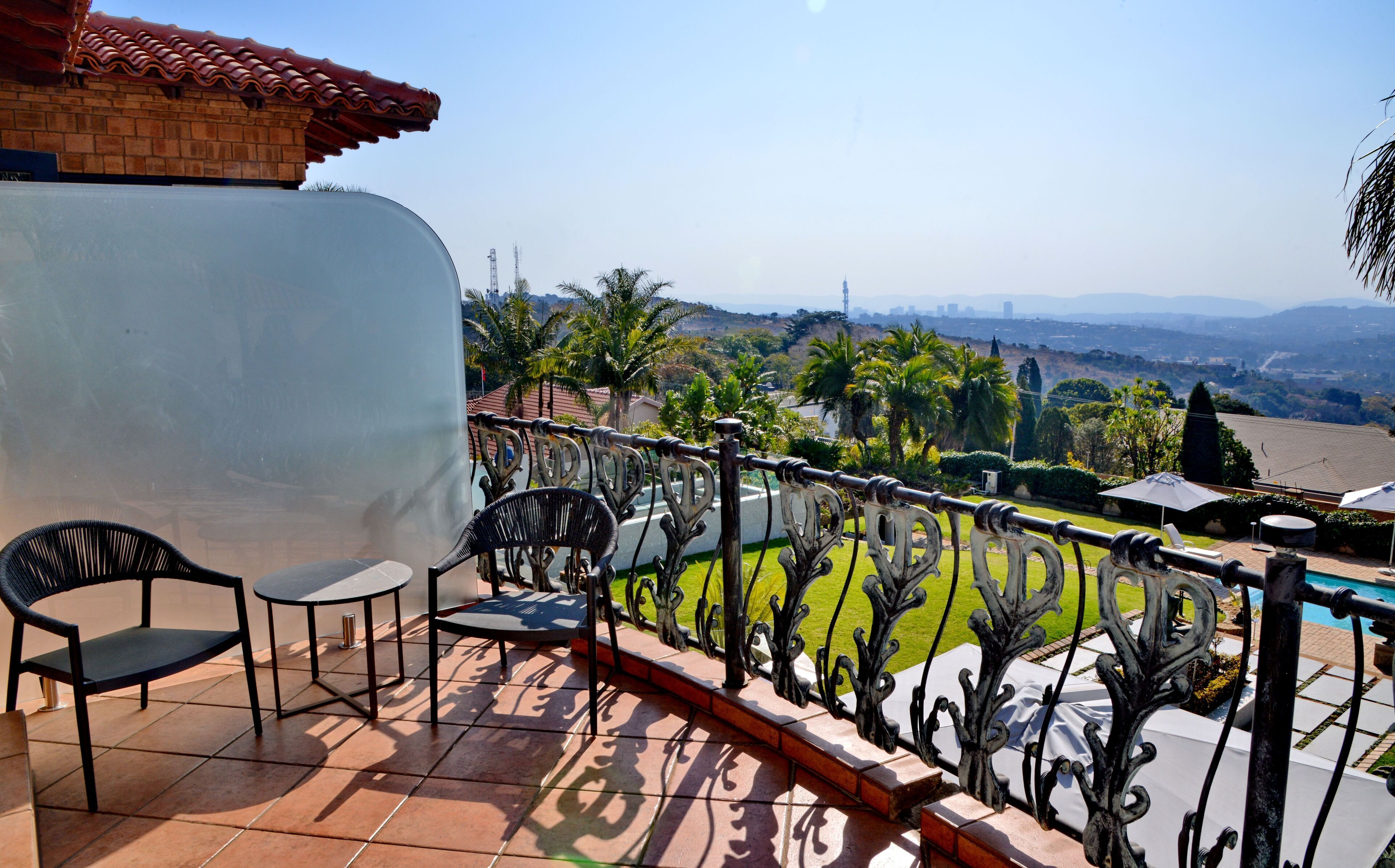 A balcony with a view of a cityscape, a pool, and a garden.