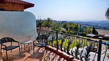 A balcony with a view of a cityscape, a pool, and a garden.