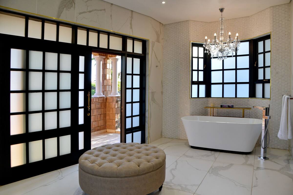 A bathroom with a freestanding bathtub, a chandelier, and a large window.