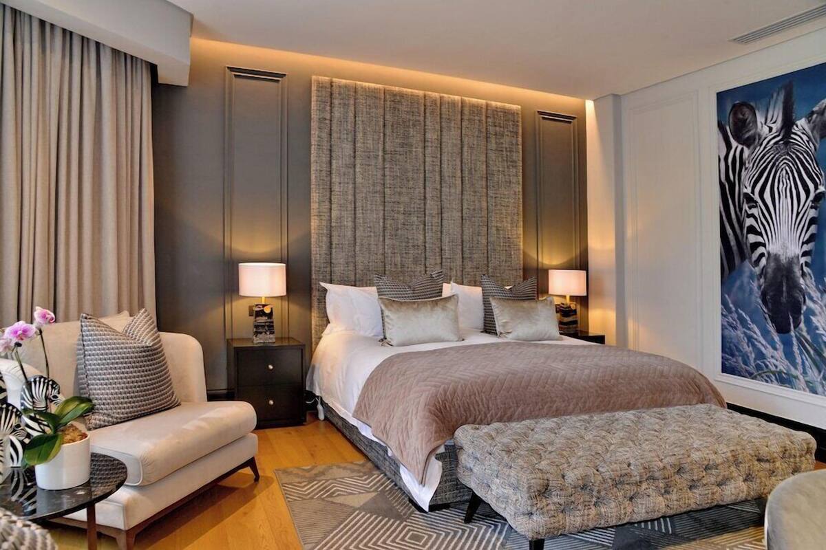 A modern hotel room with a large bed, a sofa, a small table with a lamp, and a painting on the wall.