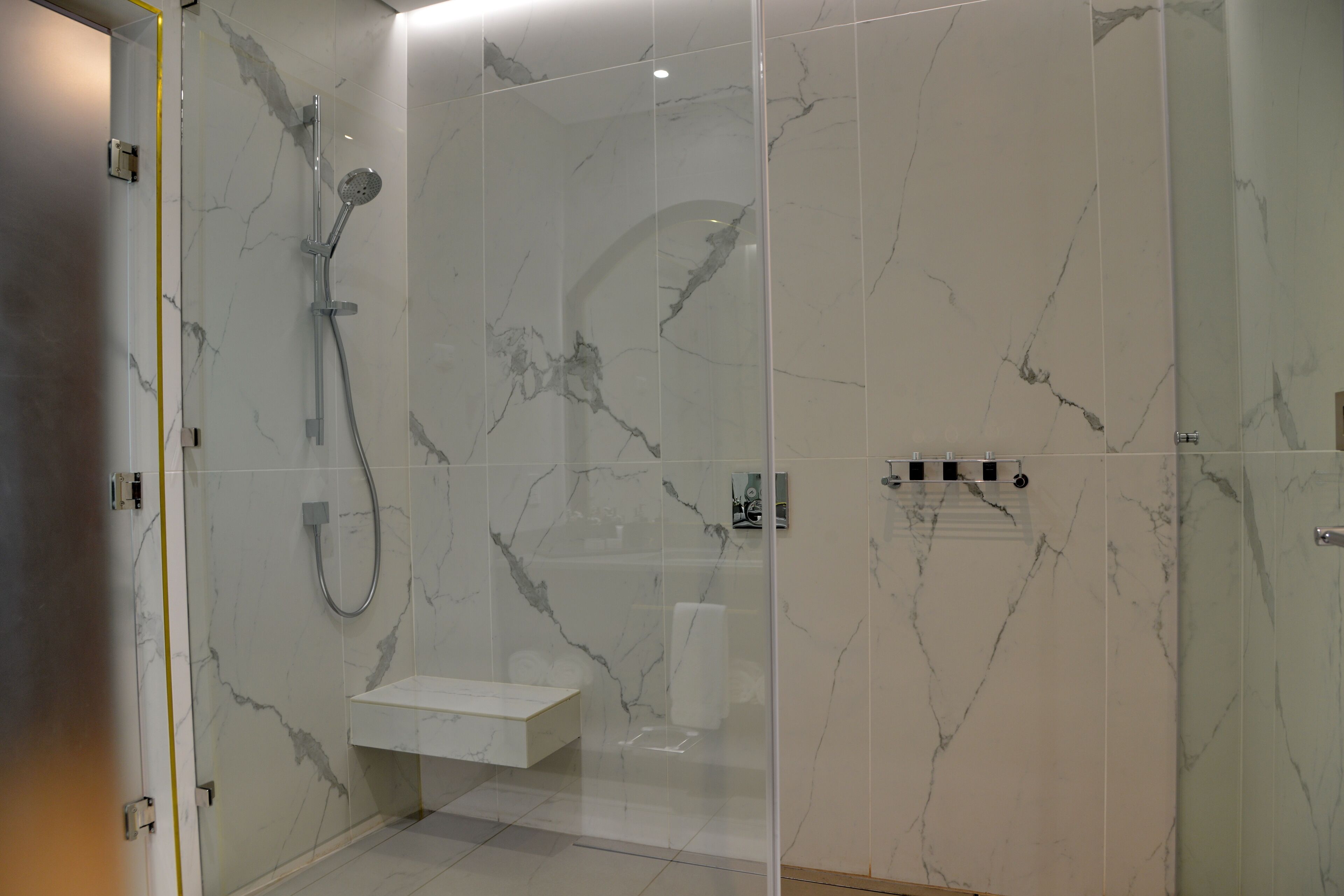 Une salle de bain moderne avec une douche à parois de verre, des murs en marbre et un lavabo blanc.