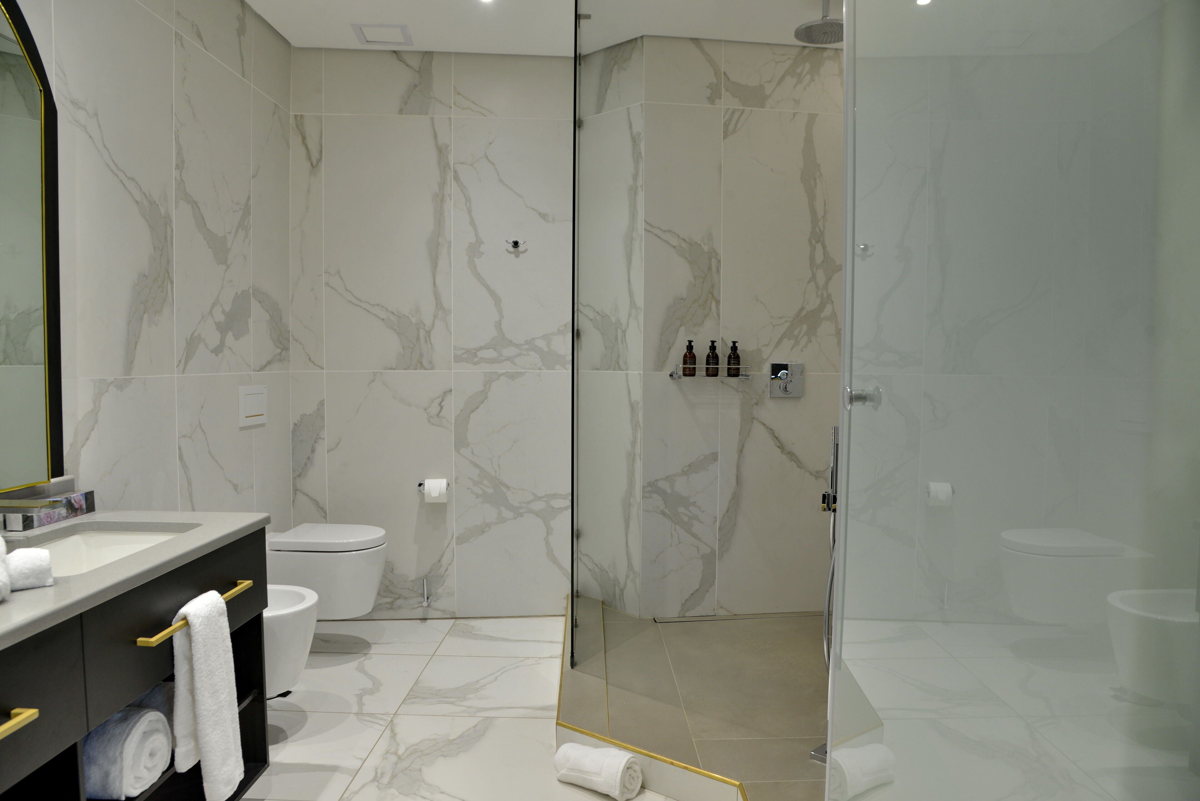 Un baño moderno con pared de mármol, cabina de ducha de vidrio y tocador con toallero.