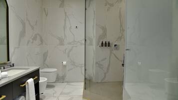 Un baño moderno con pared de mármol, cabina de ducha de vidrio y tocador con toallero.