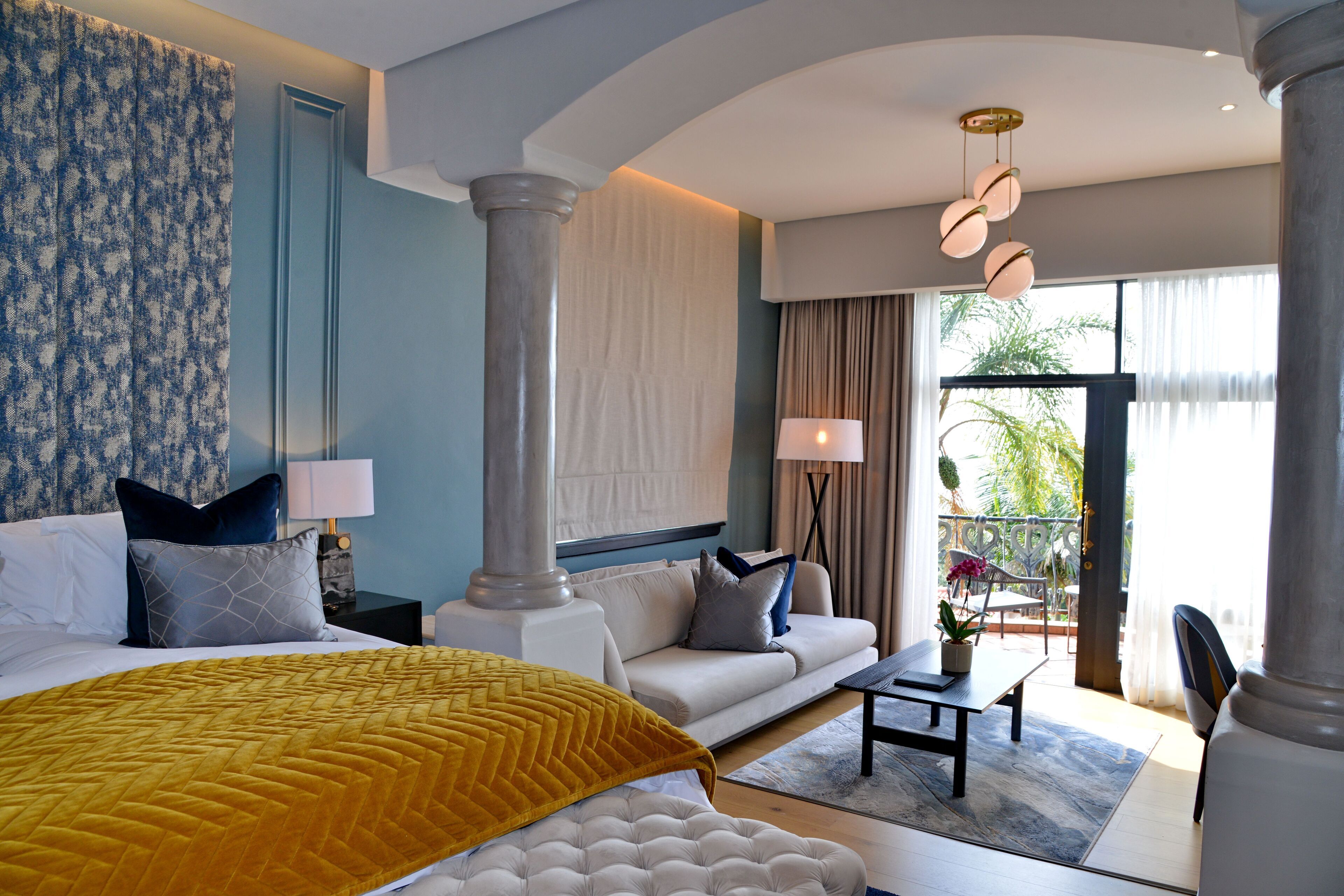 Ein Hotelzimmer mit Bett, einer Couch, einem Couchtisch und einem Balkon mit Pflanzen.