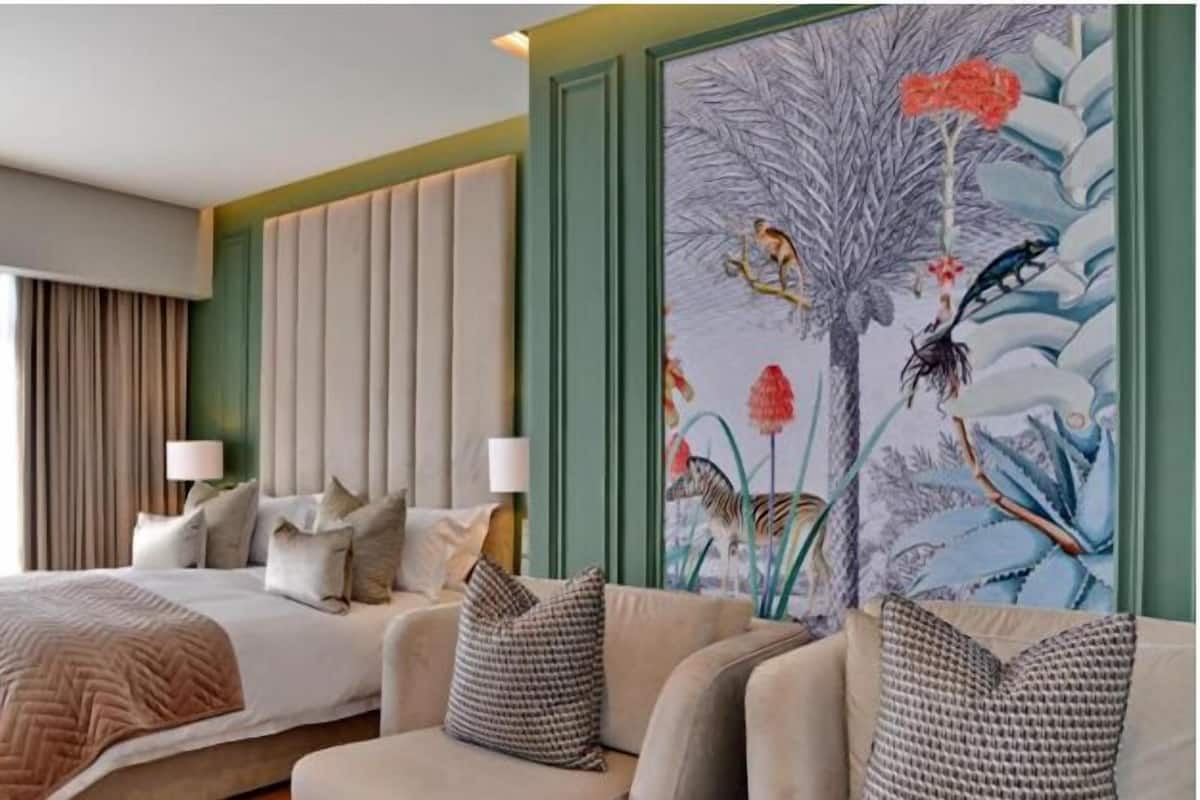 A hotel room with a bed, a sofa, a painting, and a window with curtains.