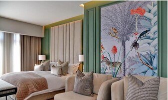 Una camera d'albergo con un letto, un divano, un quadro e una finestra con tende.