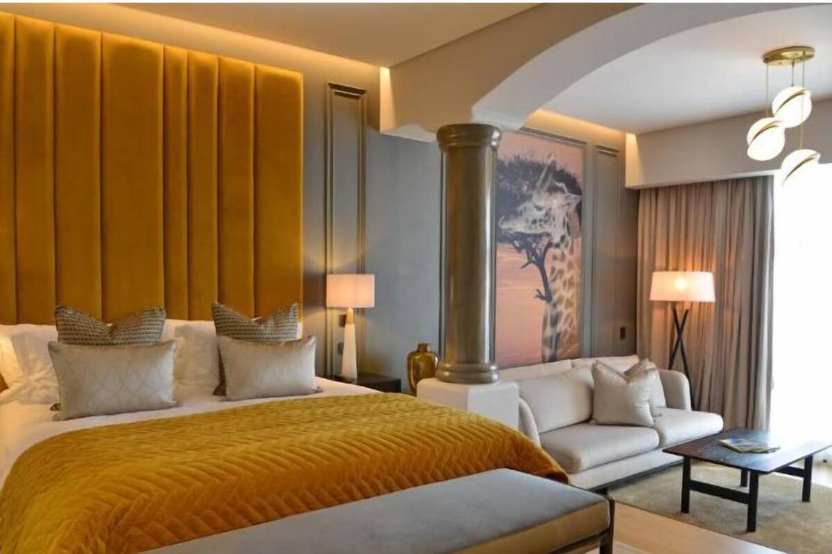 A hotel room with a large bed, a sofa, a coffee table, and a giraffe painting on the wall.