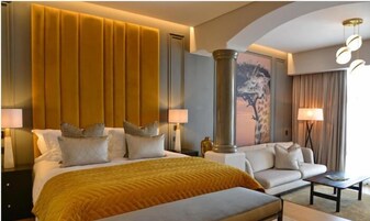 Una habitación de hotel con una cama grande, un sofá, una mesita de centro y un cuadro de una jirafa en la pared.
