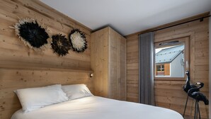 Una stanza con rivestimento in legno, un letto, decorazioni murali e vista su una casa attraverso una finestra.