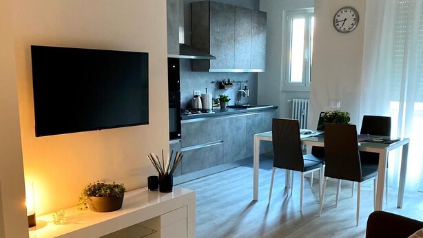 A modern living room with a flat-screen TV, a sofa, and a dining area with chairs and a table. - Tranquility and comfort in a modern and original setting! (Mantova)