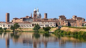 A historic building complex with a large central dome, arched walkways, and a body of water in the foreground. - Tranquility and comfort in a modern and original setting! (Mantova)