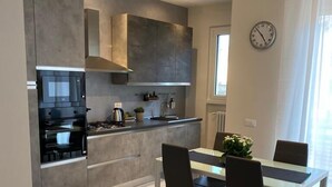 A modern kitchen with built-in appliances, a dining area with a table and chairs, and a clock on the wall. - Tranquility and comfort in a modern and original setting! (Mantova)