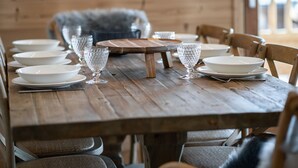 Et træspisebord dækket til seks personer med hvide tallerkner, klare glas og en midterplaceret træplanke.
