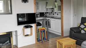 Una sala de estar con un sofá gris, un televisor, una chimenea y taburetes de colores.