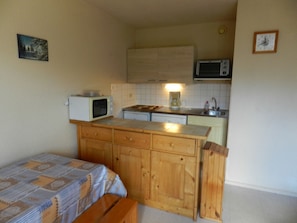 A compact kitchen with a microwave, a coffee maker, and a sink. There is a bed with a patterned bedspread in the foreground. - Ski-In/Ski-Out Apartment with Valley View, Balcony, and Easy Lift Access (Le Pleynet)