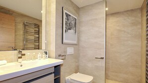 Et moderne badeværelse med et stort spejl, vask med toiletartikler, toilet og bruseområde.