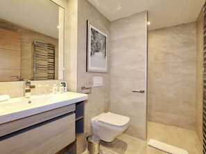 Une salle de bain moderne avec un grand miroir, un lavabo équipé de produits de toilette, des toilettes et un espace douche.