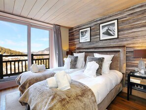 A hotel room with two beds, large windows, wooden ceiling, and mountain views.