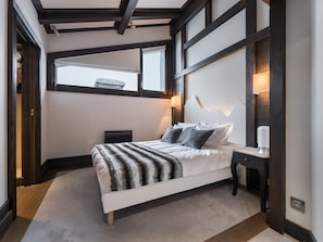 Ein modernes Schlafzimmer mit Bett, Nachttischen, Fenster und einer wandmontierten Lampe.