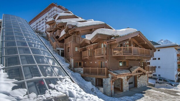 Un chalet en bois à plusieurs étages, doté de balcons et situé à proximité d’un télésiège.