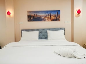 A hotel room with a bed, a headboard, a painting on the wall, and two wall-mounted light fixtures. - Pratubjai Hotel (Sattahip)