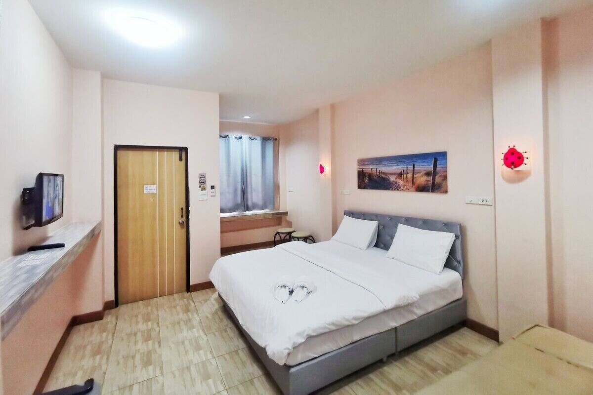 Une chambre d’hôtel avec un lit, une télévision, un bureau, une porte et une fenêtre avec des rideaux.