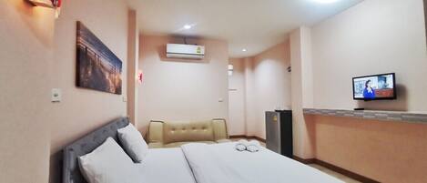 A hotel room with a bed, a television, a wall-mounted air conditioner, and a painting.