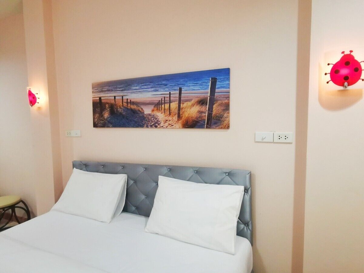 A bedroom with a bed, a wall-mounted painting of a beach scene, and two wall-mounted light fixtures.