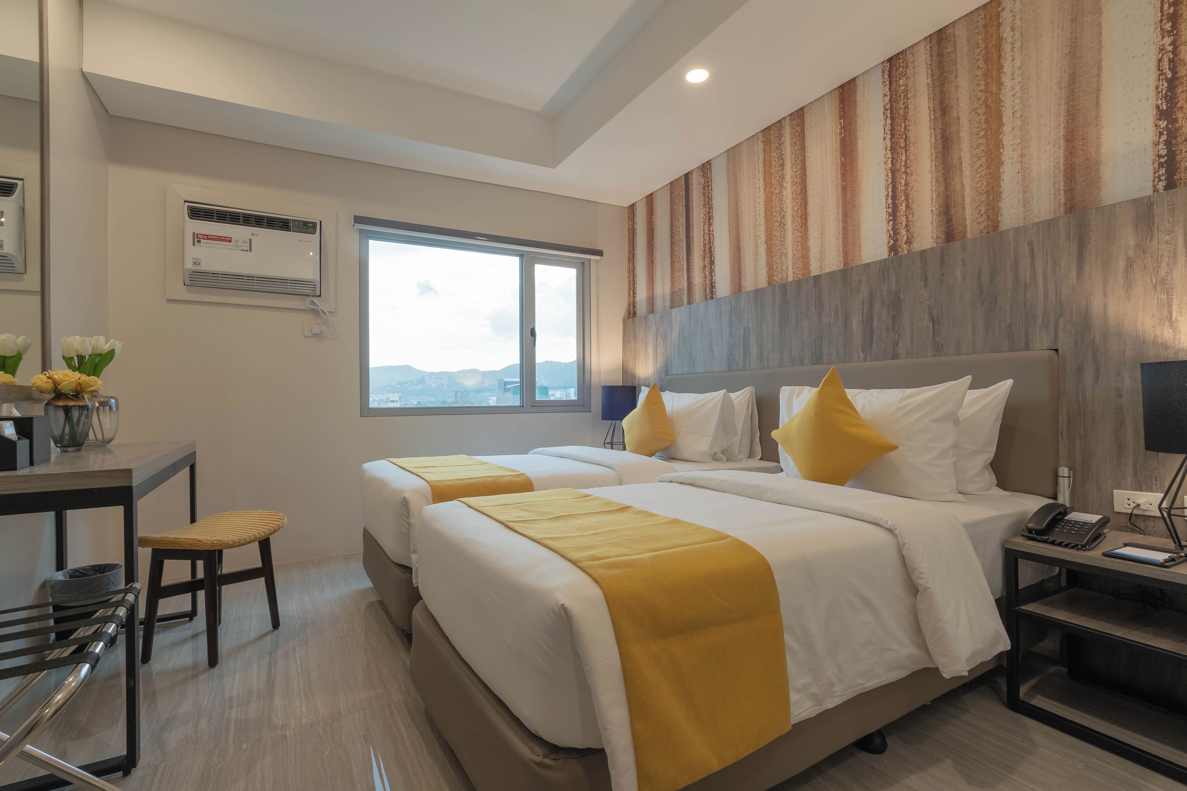 Una habitación de hotel con dos camas, un escritorio y una silla, un ventanal con vistas y un equipo de aire acondicionado.