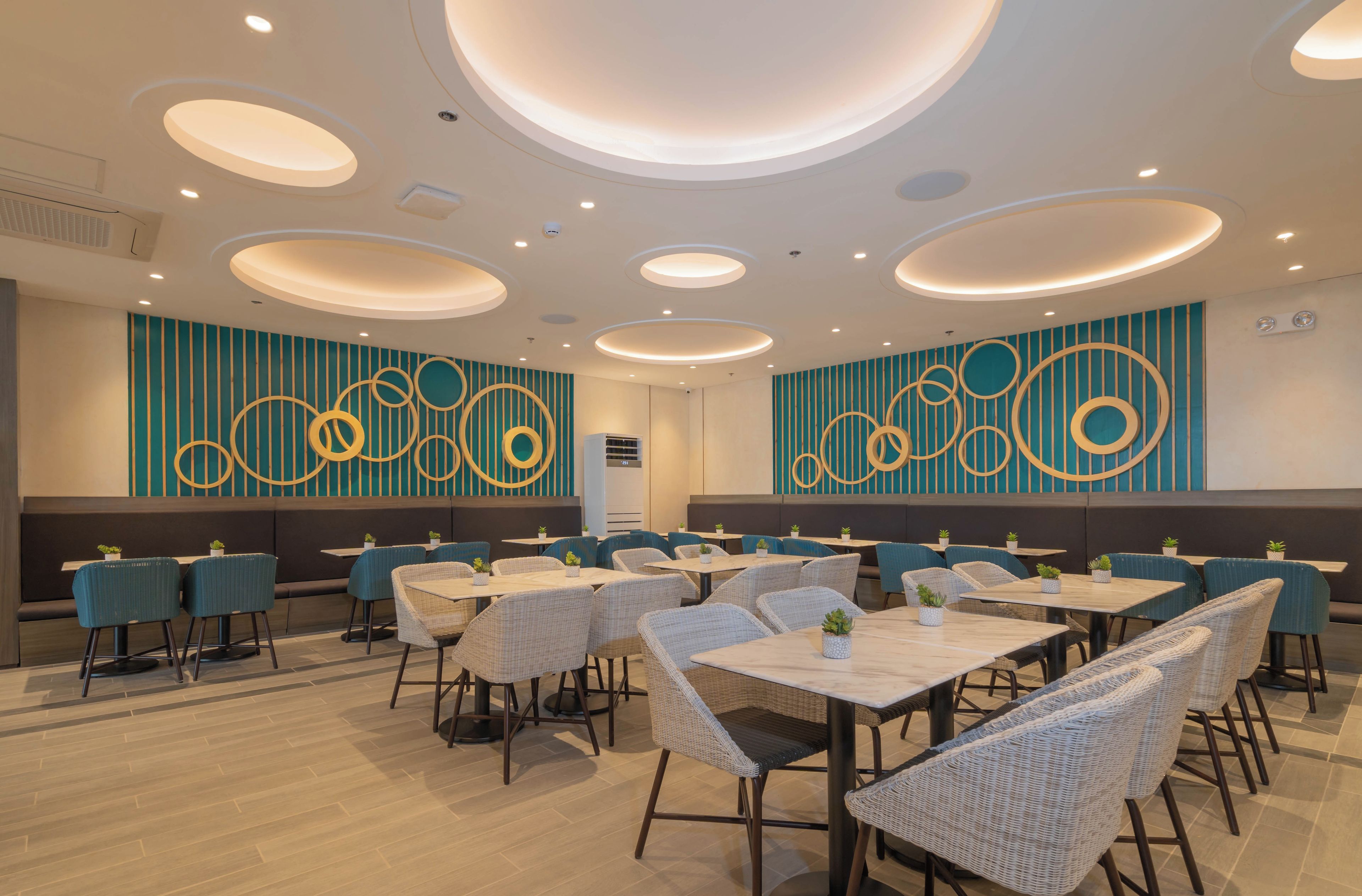 A modern restaurant with round tables and blue chairs, featuring a teal and gold wall design.