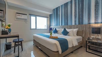 Une chambre d’hôtel moderne avec un grand lit, un bureau avec une chaise, une petite table agrémentée de fleurs et une grande fenêtre.