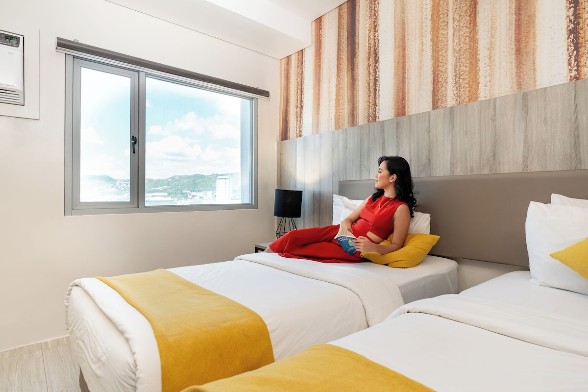 A hotel room with two beds, a large window, and a view of the cityscape.