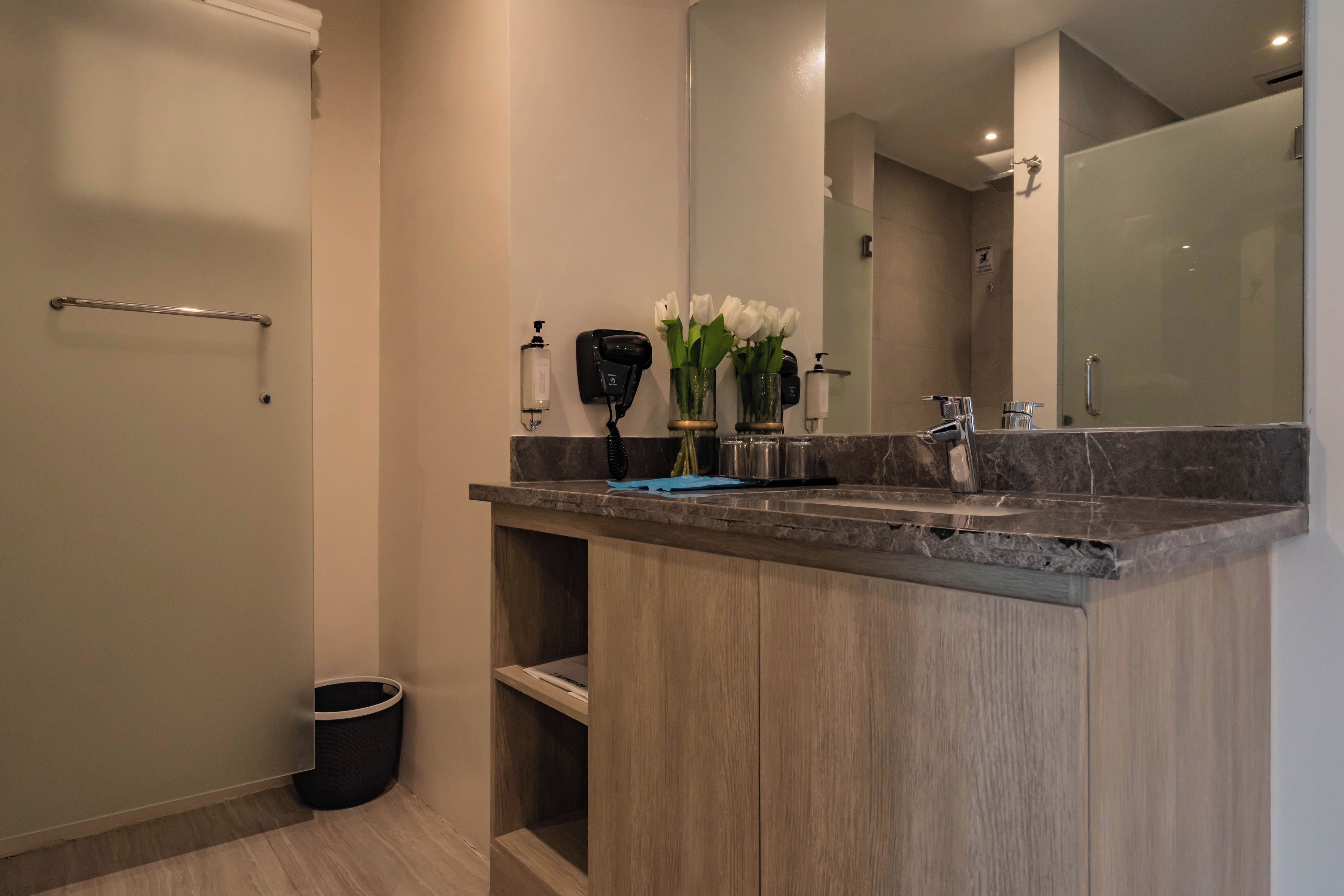 A modern bathroom with a marble countertop, a handheld showerhead, and a large mirror.