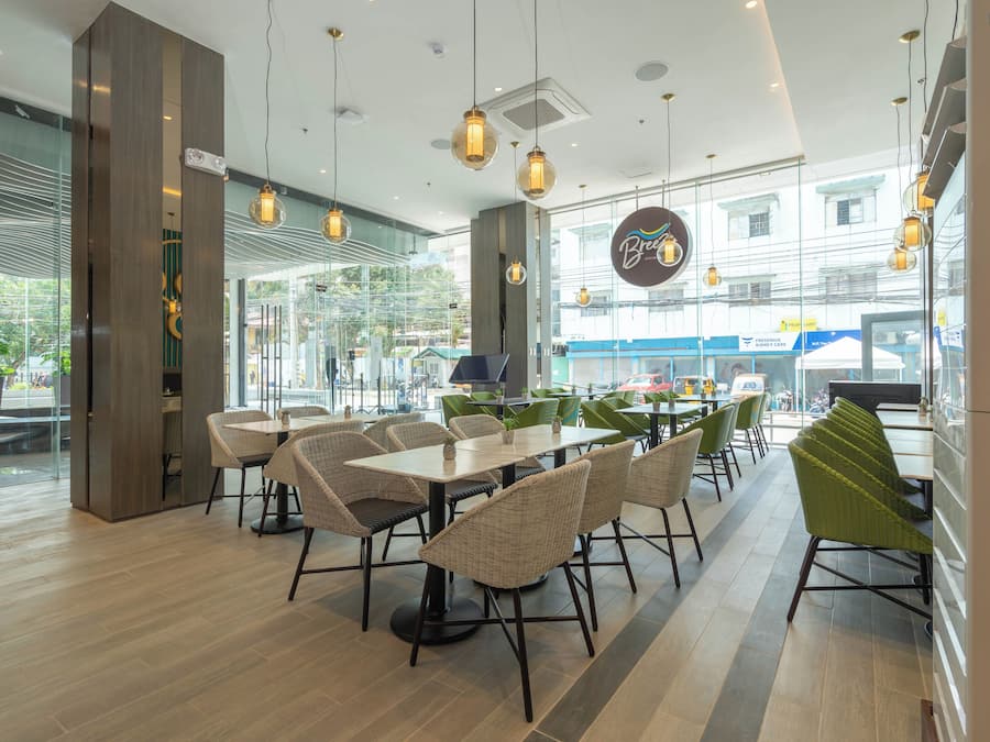 A modern restaurant interior with wicker furniture, pendant lighting, and large windows offering a view of the street.