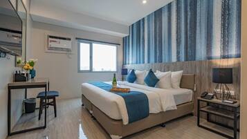 Una habitación de hotel moderna con una cama grande, un escritorio con una silla, una mesita pequeña y una mesita de noche con una lámpara.
