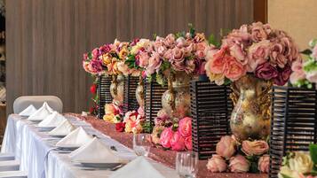 A long dining table set with white tablecloths, multiple place settings, and floral centerpieces in gold vases.