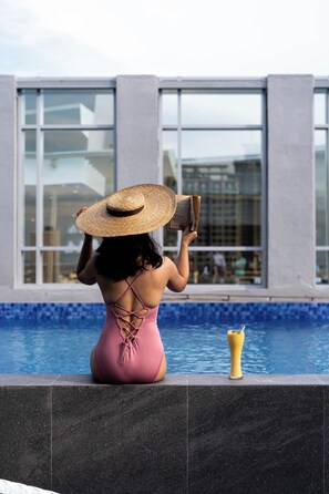 A person sitting by a pool with a drink, wearing a hat and reading a book. - Bayfront Hotel Cebu - Capitol Site (Cebu City)