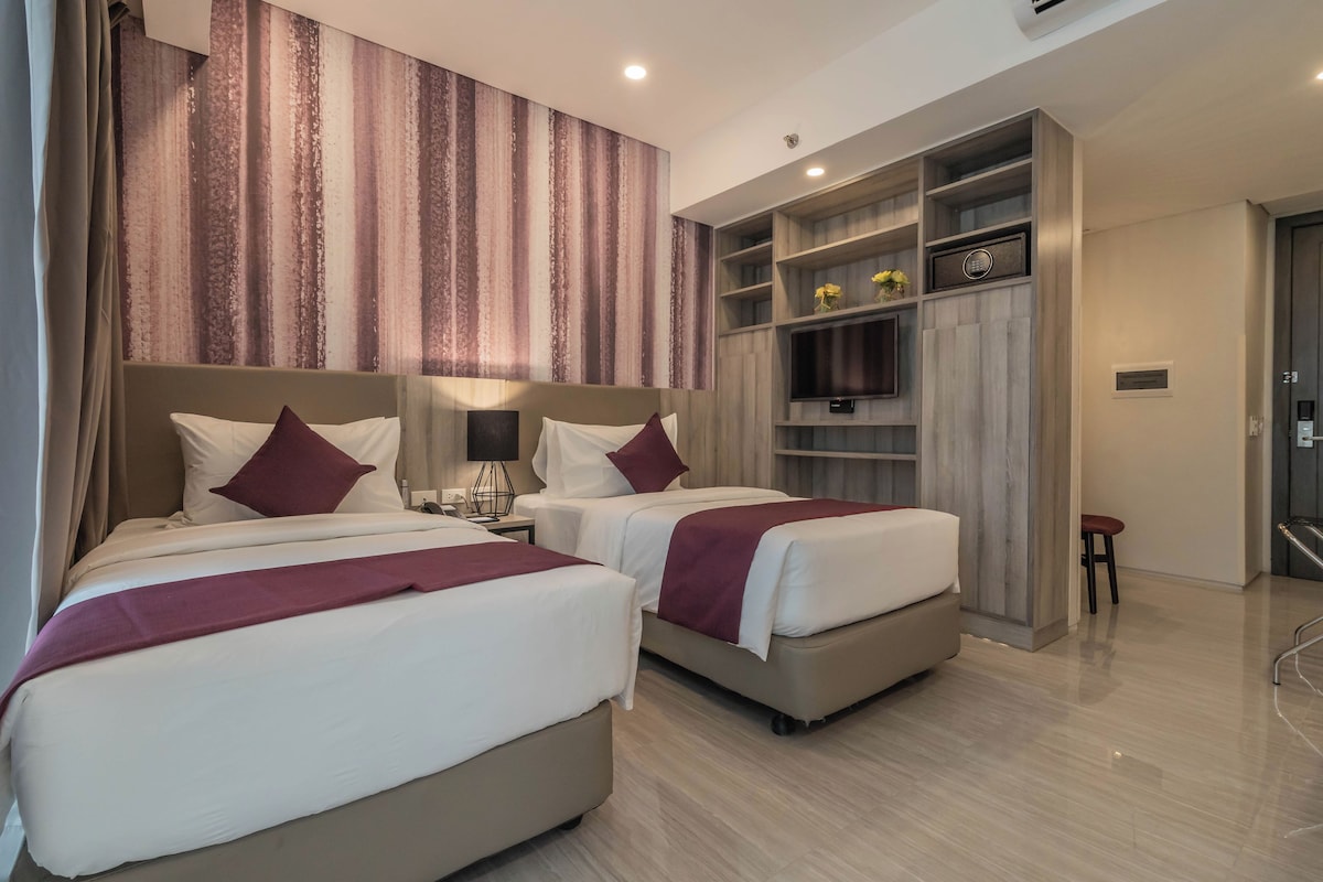 A hotel room with two beds, a desk, a TV, and a wardrobe.
