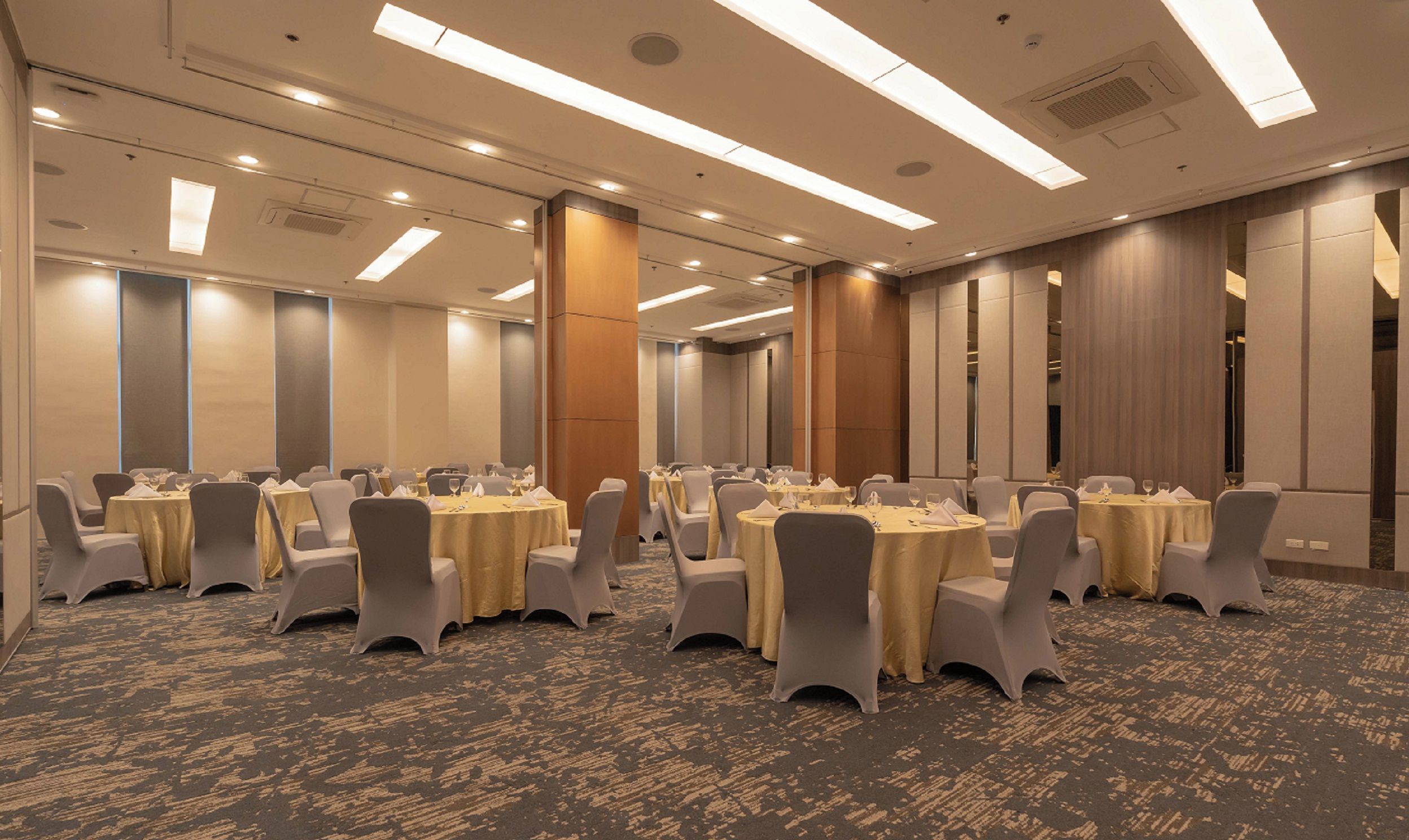 A conference room with multiple round tables, chairs, and a carpeted floor.