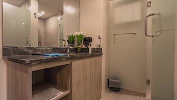 A modern bathroom with a marble countertop, a mirror, a towel rack, and a shower area.
