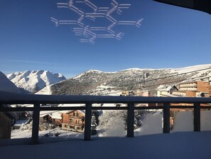 A snowy mountain landscape with a clear sky, a wooden building with multiple balconies, and a snow-covered ground.