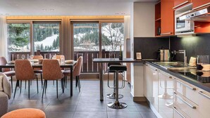 Une cuisine moderne avec un coin bar, de grandes fenêtres donnant sur un paysage enneigé et un espace repas avec des chaises et une table.